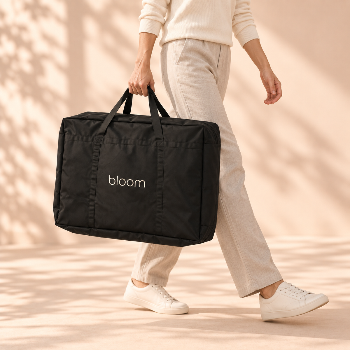 Bloom Recovery Mat in its packed black carry bag, carried in one hand at the side while walking — illustrative scale