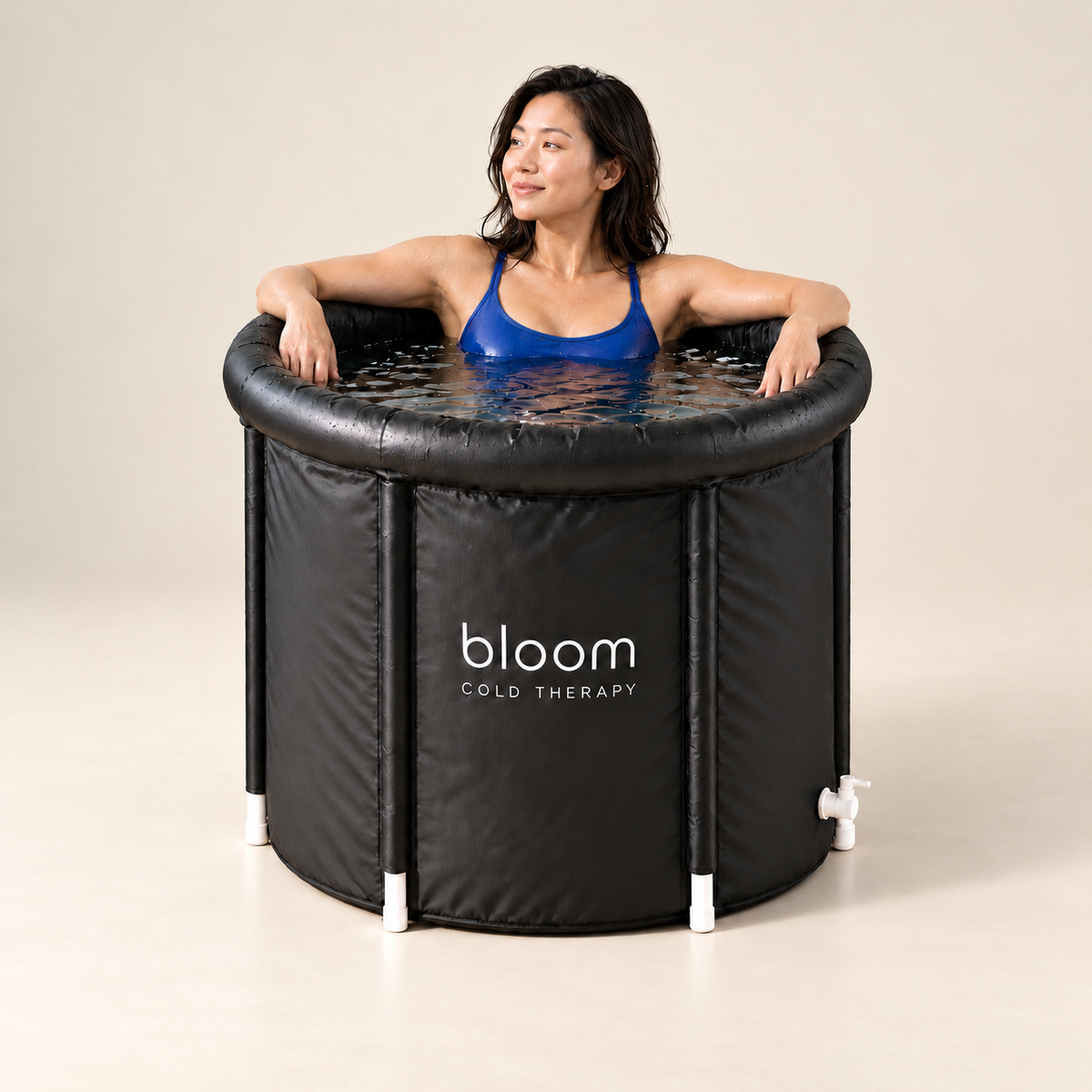 Woman in blue swimwear relaxing in the Bloom Ice Core tub on a soft ivory studio backdrop.